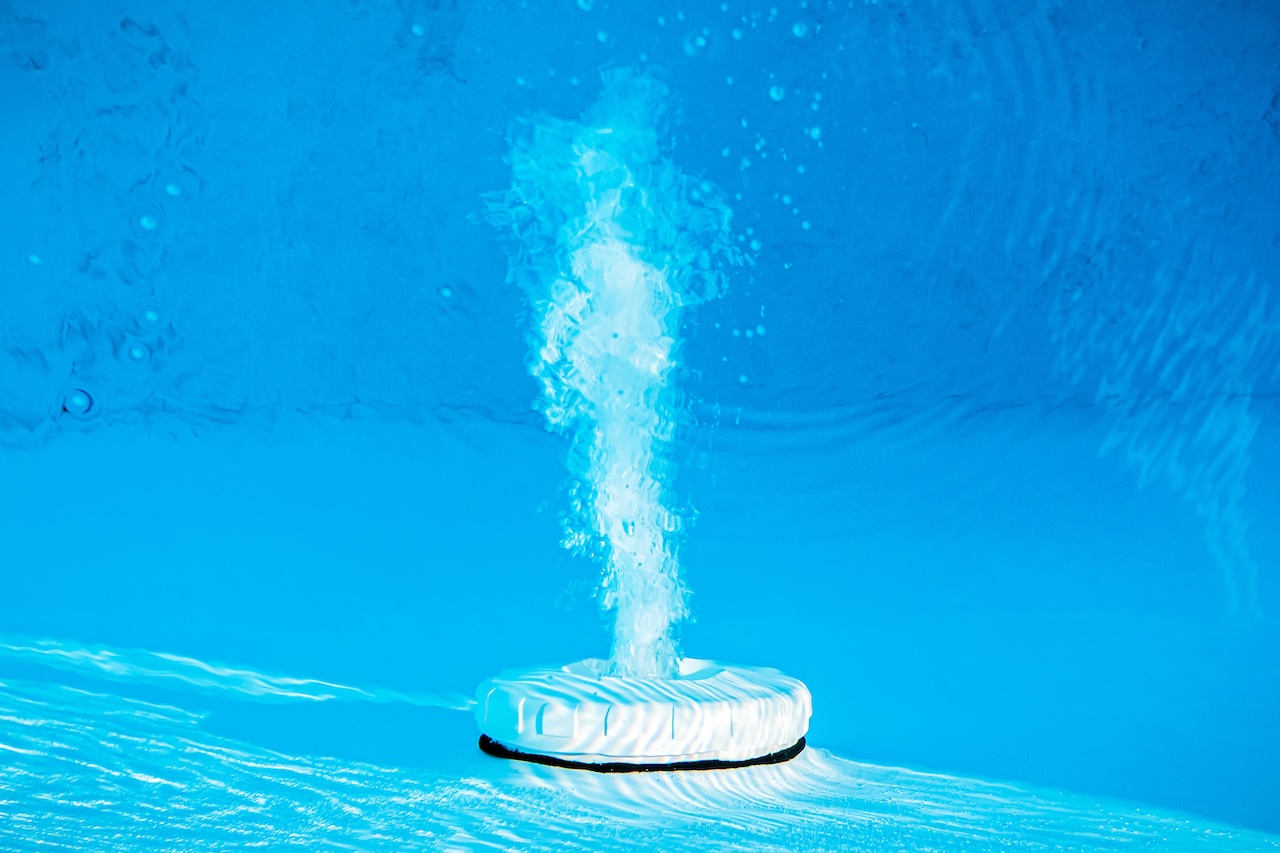 Top view of an active underwater discharge nozzle device equipment set in a blue swimming pool.