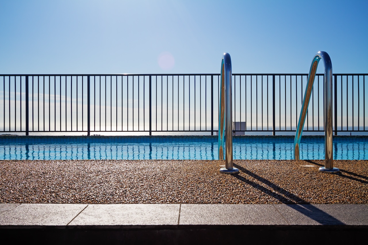 Swimming pool edge with ladder, fence and sky background