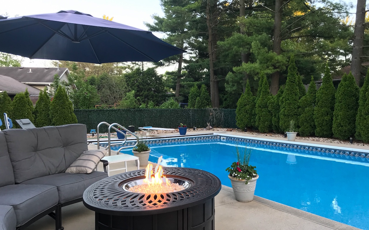 backyard pool with firepit and privacy bushes at dusk